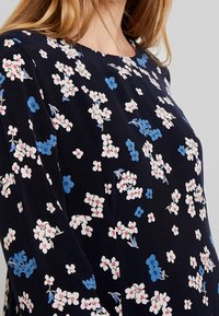 Marinblus med ett blommönster i vitt och blått. Har rund halsringning och lös passform. Tillverkad av lättviktig tyg.