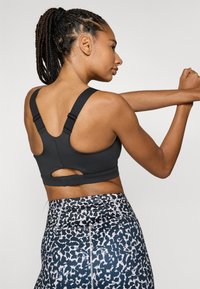 Svart sportsbh med brede stroppar og detalj med utskjæring på baksiden. Bærast med mønstrede tights med blå og kvite abstrakte design.