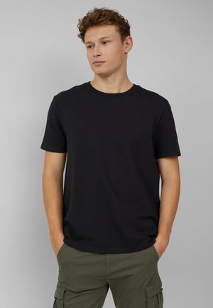 Zwarte T-shirt met korte mouwen van een gestructureerde stof en een ronde hals. Gecombineerd met groene cargobroeken die een relaxte pasvorm en casual ontwerp hebben.