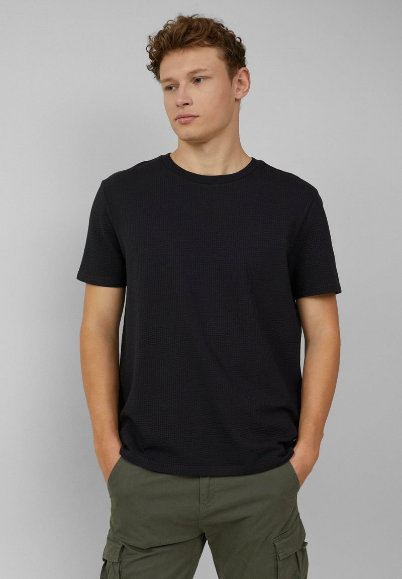 Zwarte T-shirt met korte mouwen van een gestructureerde stof en een ronde hals. Gecombineerd met groene cargobroeken die een relaxte pasvorm en casual ontwerp hebben.