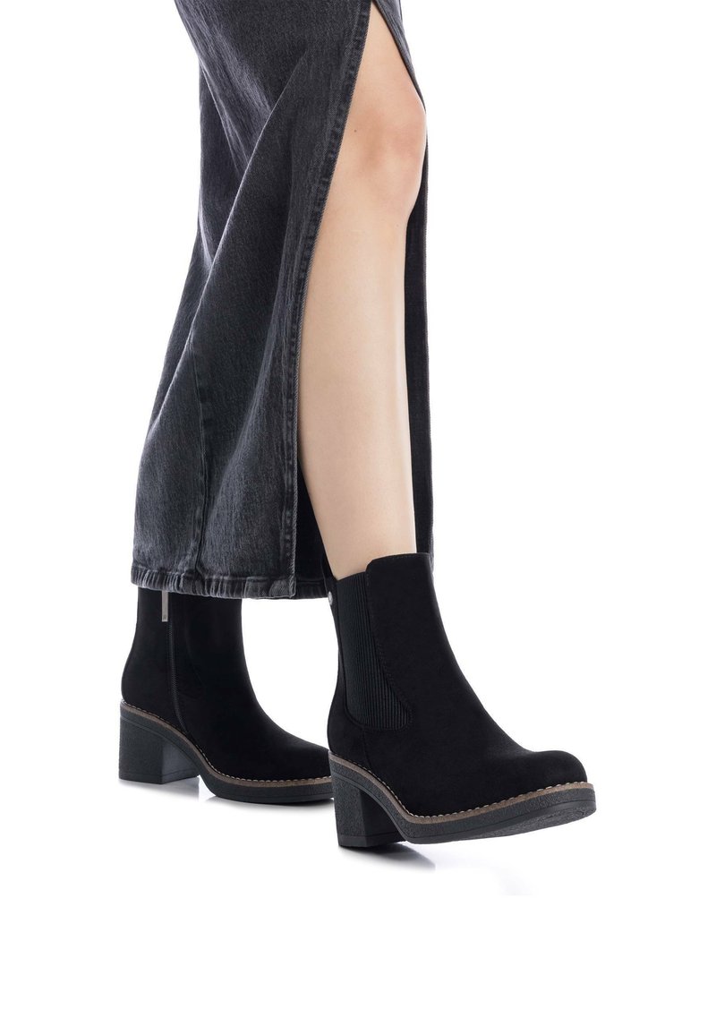 Stivaletti alla caviglia in suede nero con tacco grosso e pannelli laterali in elastico. Indossati con una gonna in denim nera con una fessura laterale.