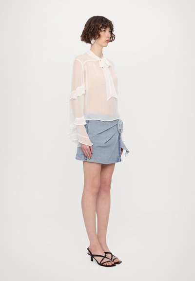 Lettet, gennemsigtig hvid bluse med volangærmer og en sløjfe i kraven, parret med en blå denim mini-skirt med knudedetalje i siden.