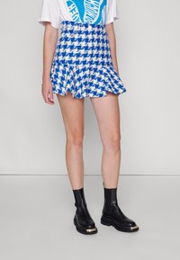 Mini falda de cuadro de pato azul y blanco con dobladillo acampanado, combinada con botas negras de tobillo con un acento de hardware dorado.