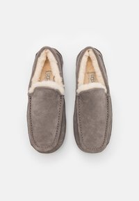 Szürke nubuk slip-on papucsok puha barna gyapjúbéléssel és varrott részletekkel az éleken. Kerek orrú dizájn. Nincs látható fémalkatrész.