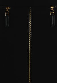 Jupe noire avec une fermeture éclair centrale dorée dotée d'une tirette en boucle et d'accents en cuir de chaque côté. Texture lisse et design ajusté.