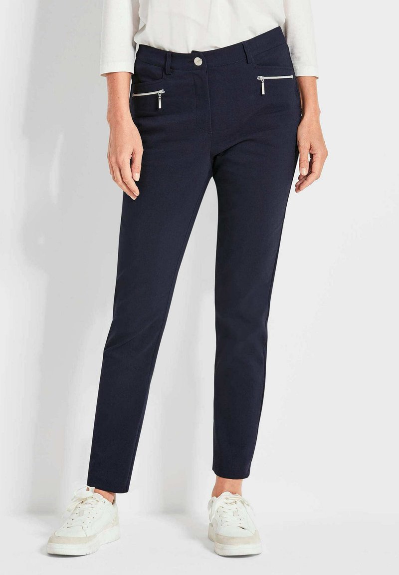 Dunkelblaue Slim-Fit-Hosen aus Stretchstoff, mit zwei Reißverschlusstaschen vorne und klassischem Knopfverschluss. Anlassgerecht zu weißen Sneakers getragen.