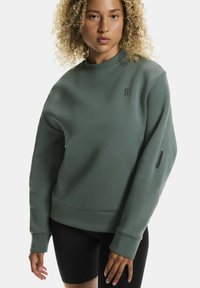 Roheline džemper, millel on ümmargune kaelus, ribaga mansetid ja väike logo rinnal. Kraed on musta aktsendiga varrukal.