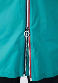 Giacca turchese con cerniera centrale dotata di tiretto argentato e dettagli a contrasto in rosso e blu navy lungo le linee della cerniera, con una texture liscia.