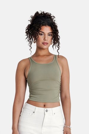 Olive green ribbed cropped tank top with ruched sides and wide straps, paired with high-waisted white jeans and simple jewelry accents.