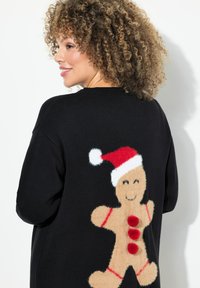 Zwarte trui met een ontwerp van een peperkoeken man op de achterkant, met rode accenten, drie pompons en een rood hoedje met witte punt. Gemaakt van polyester.