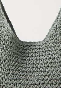 Sac à épaule en tricot gris avec une texture à mailles larges, une forme arrondie et un design d'ouverture incurvée. Matériau léger et flexible.