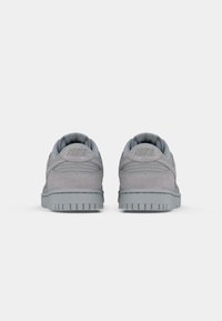 Grå semsket joggesko med en jevn tekstur, polstret krave og Nike-logo på hælen. Har en flat gummisåle med et strukturert mønster.