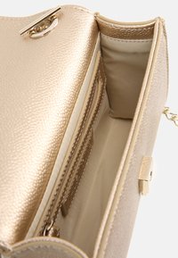Interno della borsa con texture dorata, dotato di tasca con zip, diversi slot per carte e una fodera liscia. Caratterizza hardware metallico e chiusura a gancio.