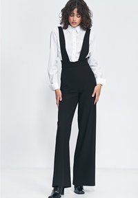 Czarne spodnie z wysokim stanem, szerokimi nogawkami i szelkami, zestawione z białą koszulą zapinaną na guziki. Gładki materiał z dopasowanym krojem.