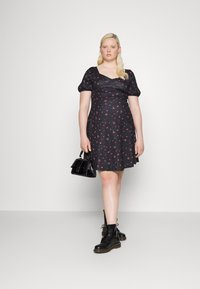 Vestido preto com estampa floral, mangas curtas bufantes, corpete justo e saia rodada. A modelo usa botas de combate pretas e segura uma minibag.