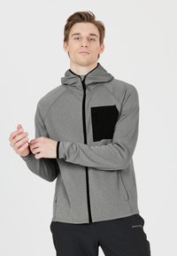 Grauer Reißverschluss-Hoodie mit einer schwarzen Brusttasche, aus strukturiertem Stoff gefertigt. Verfügt über eine Kapuze, einen Frontreißverschluss und Raglanärmel.