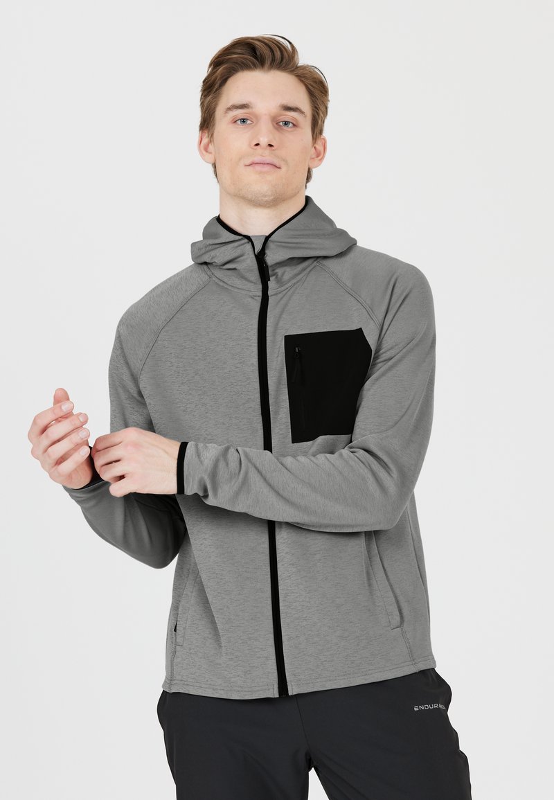 Grauer Reißverschluss-Hoodie mit einer schwarzen Brusttasche, aus strukturiertem Stoff gefertigt. Verfügt über eine Kapuze, einen Frontreißverschluss und Raglanärmel.