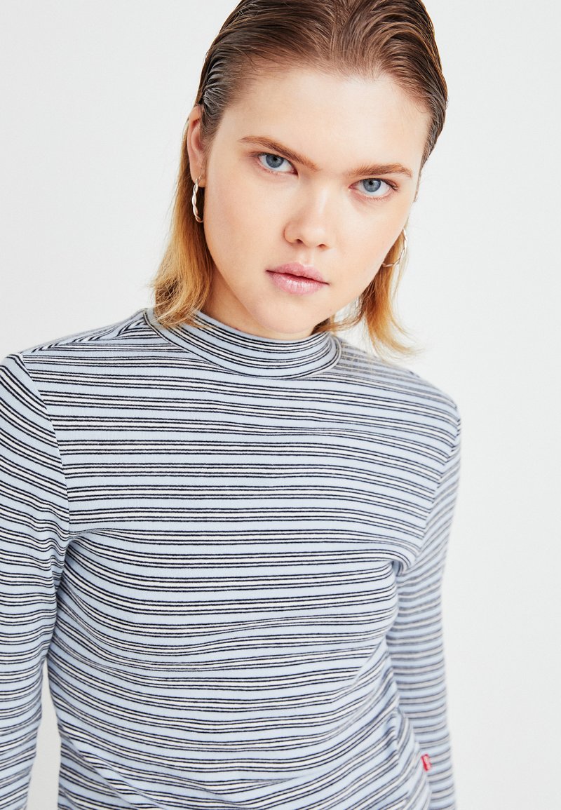 Gestreiftes Langarmshirt in Blau und Weiß, mit hochgeschlossenem Kragen und weichem Stoff. Enthält ein kleines rotes Logo-Detail am Saum.