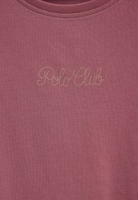 Tela malva con pequeños tachones metálicos que forman el texto en cursiva "Polo Club" cerca del escote.