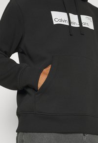 Calvin Klein Jeans HYPER REAL BOX LOGO GENDERLESS UNISEX - Jersey con capucha - black