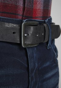 Zwarte leren riem met een rechthoekige zilveren gesp, gedragen over donkerblauwe denim, met een subtiele vervaagde textuur en contrasterende stiksels.