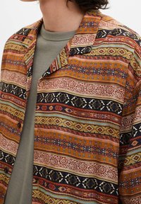 Kortærmet skjorte med et indviklet, flerfarvet geometrisk mønster i brune, røde og blå nuancer på et let stof.