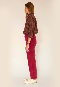 Chemise à carreaux multicolore en vert foncé, bordeaux et rose, associée à un pantalon en velours côtelé bordeaux et des baskets en toile beige.