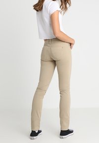Béžové skinny džíny z bavlněné směsi, s pasem střední výšky, zadními kapsami a decentními detaily šití. Černé tenisky doplňují celkový vzhled.
