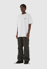 Hvid oversized t-shirt med lille logo på brystet, parret med løstsiddende sorte cargo-bukser med sidelommer og struktureret stof.