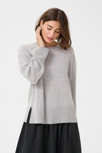 Svetlo siva pletena pulover s okroglim ovratnikom, stranskimi razporki in rebrastimi manšeti. Mehka tekstura in sproščen kroj, kombiniran z črno krilom.