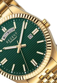 Montre en or avec un cadran texturé vert, des index horaires blancs, trois aiguilles dorées et une fenêtre de date. Elle est dotée d'un bracelet en maillons dorés.