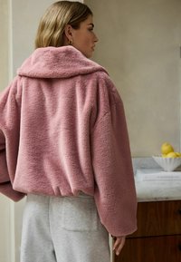 Lækkert pink jakke med bred krave og voluminøse ærmer, parret med lyse grå sweatpants. Blød tekstur og afslappet pasform.