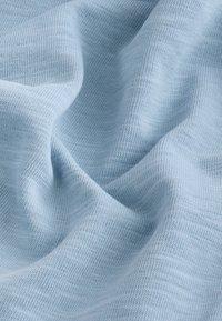 Tissu bleu clair à la texture lisse, présentant un motif fin tricoté et un drapé doux, créant des plis et des contours subtils.