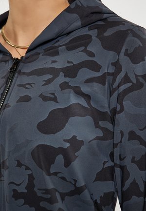 Fekete és kék camo mintázatú cipzáros kapucnis pulóver, sima textúrával és kapucnival. Közelkép a cipzár részletéről és az anyag mintázatáról.