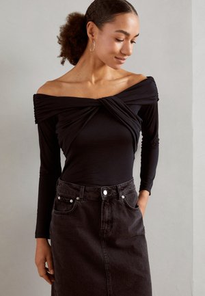 Black off-the-shoulder long-sleeve top with gathered fabric at the bust, paired with a high-waisted black denim skirt featuring button closure.