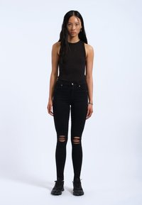 Top negro sin mangas combinado con unos pantalones ajustados negros de tiro alto que presentan desgarros en las rodillas, completado con zapatillas negras. Diseño simple y ajustado.