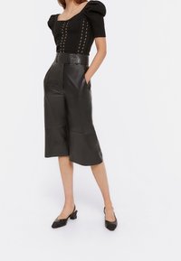 Top nero con maniche a sbuffo e design a trecce, abbinato a culotte in pelle nere a vita alta con tasche frontali e gamba larga.
