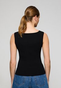 Svart ribbad linne med en figurnära siluett och breda axelband, parat med högmidjade blå denimshorts.