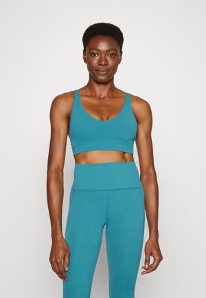 Sutiã desportivo em azul petróleo com decote em forma de U, combinado com leggings de cintura alta em azul petróleo. Textura suave e detalhes de costura mínimos.