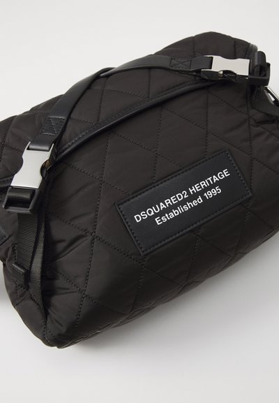 Czarna pikowana torba z nylonu z regulowanym czarnym paskiem, srebrnymi detalami i teksturowaną etykietą z napisem "DSQUARED2 HERITAGE Established 1995."