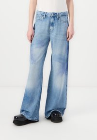 Jeans de denim azul claro acampanados con una cintura alta, que presentan acentos azules en un estilo acuarela y un clásico diseño de cinco bolsillos.