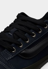 Σκούρο μπλε σουέντ αθλητικό παπούτσι με μαύρα κορδόνια, μεταλλικά περβάζια και υφή δερμάτινου διακοσμητικού στοιχείου. Διαθέτει ορατές ραφές και σχεδιασμό με χαμηλό προφίλ.