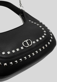 Borsa a spalla in pelle nera con accenti di borchie argentate e un logo metallico prominente. La borsa ha una forma curva con una finitura testurizzata.
