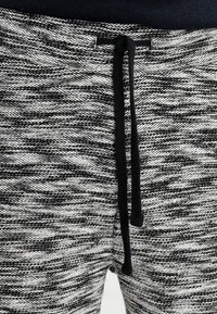 Gros plan sur un pantalon de jogging noir et blanc texturé avec un cordon noir noué à la taille.