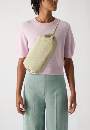 Mintgrøn stof crossover taske med en rund form, samlet top og subtil tekstur. Båret over en lys pink sweater og stribede bukser.
