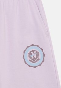 Lyse lilla bomullssweatpants med en sirkulær blå og grå logo med teksten "N" og "72", dekorative detaljer og en sidelomme.