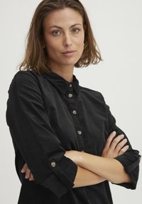 Sort kordfløjlsskjorte med krave, knaplukning foran og opsmøgede ærmer med knappede manchetter. Blød tekstur, afslappet pasform.