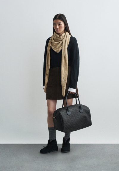 Maglione nero, sciarpa beige, gonna marrone, calze grigie e stivali neri; porta una grande borsa a tracolla marrone con manici neri.