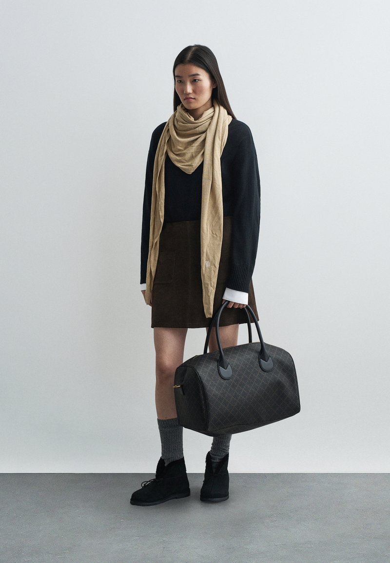 Un pull noir, une écharpe beige, une jupe marron, des chaussettes grises et des bottes noires ; portant un grand sac à main brun à motifs avec des poignées noires.