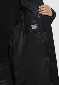 Sorte isolerede jakke med en glat overflade, lynlåslomme og et logo-patch. Blødt inderfore med knaplukning.